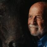 Portrait of an elderly man sharing a moment with a bison in dim lighting.