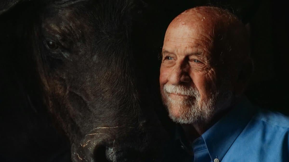Portrait of an elderly man sharing a moment with a bison in dim lighting.