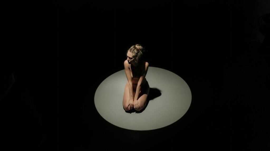 A woman kneeling in the spotlight, creating an introspective mood.