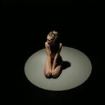 A woman kneeling in the spotlight, creating an introspective mood.