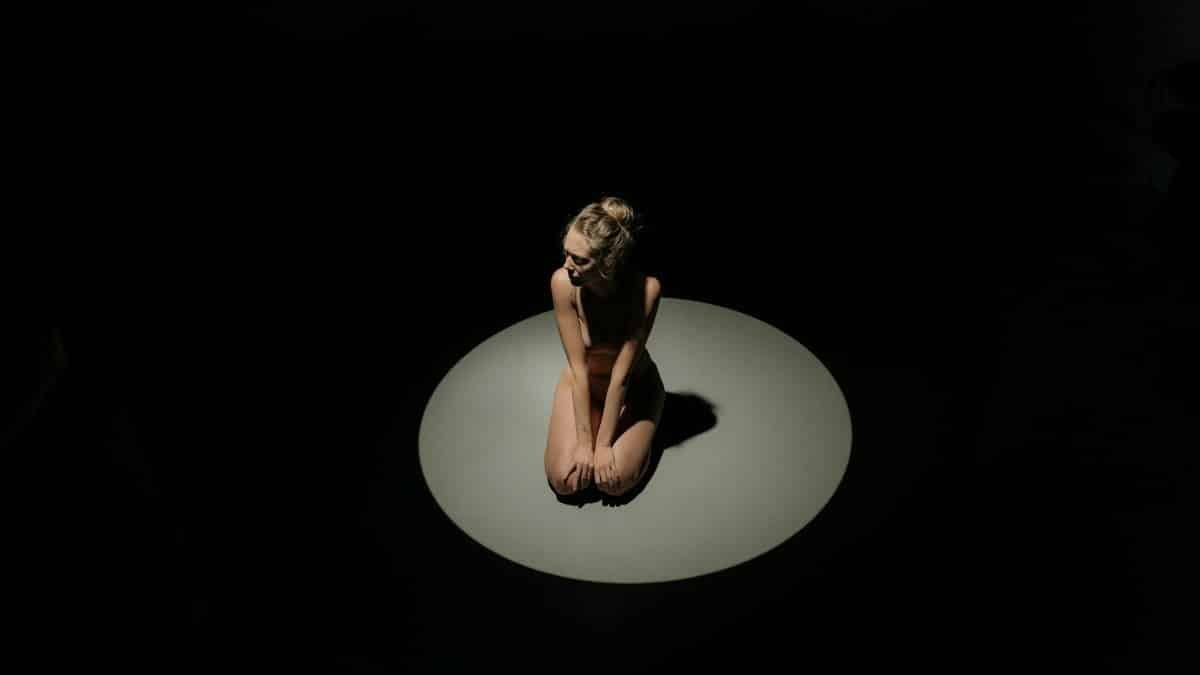 A woman kneeling in the spotlight, creating an introspective mood.