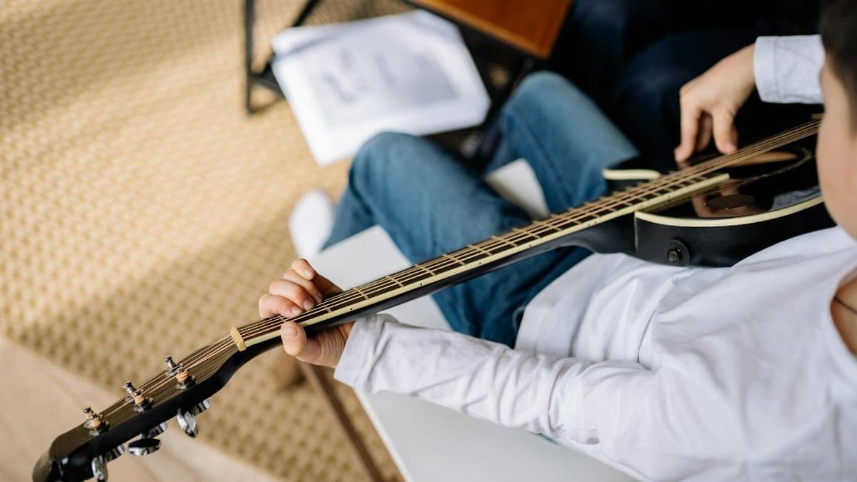 A child sitting and playing an acoustic guitar indoors in a close-up view.