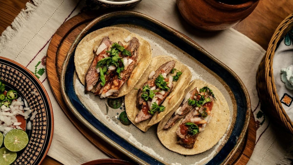 Three delicious steak tacos topped with onions and cilantro, served on a rustic platter.