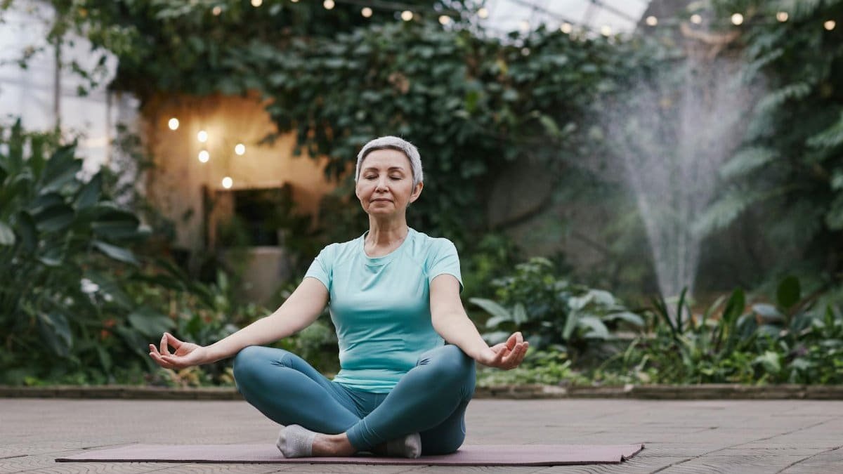 Elderly woman meditating in serene botanical garden setting, focused on wellness and mindfulness.