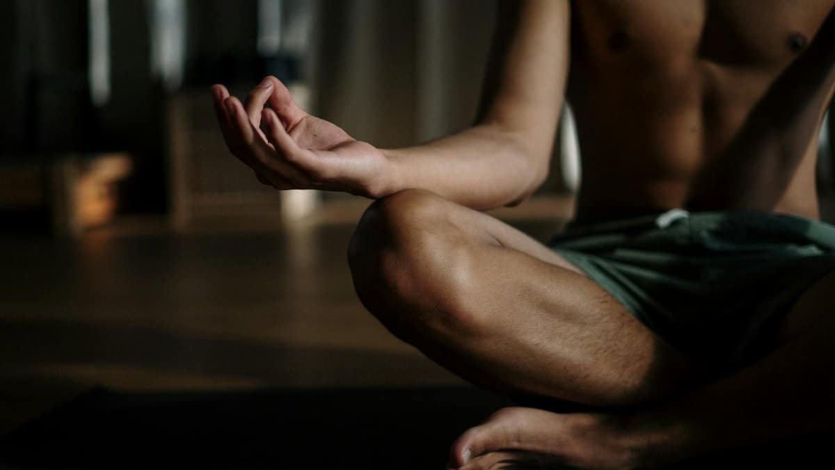 A shirtless man in a yoga studio meditating in the lotus position for relaxation and wellness.