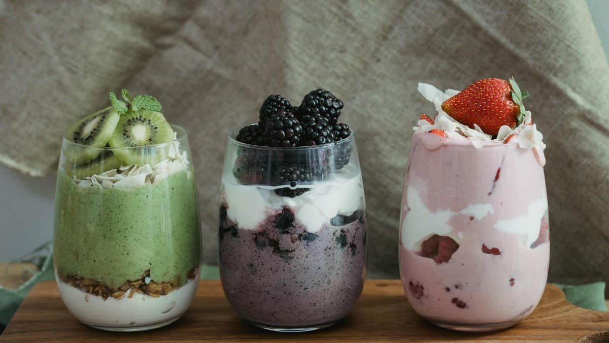 Delicious yogurt parfaits with kiwi, blackberries, and strawberries on a wooden board.