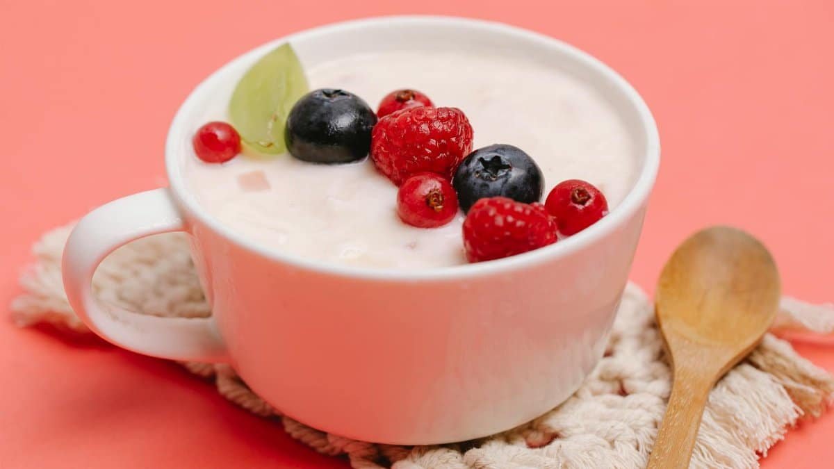 Top view of a white cup filled with yogurt and assorted berries on a pink background.