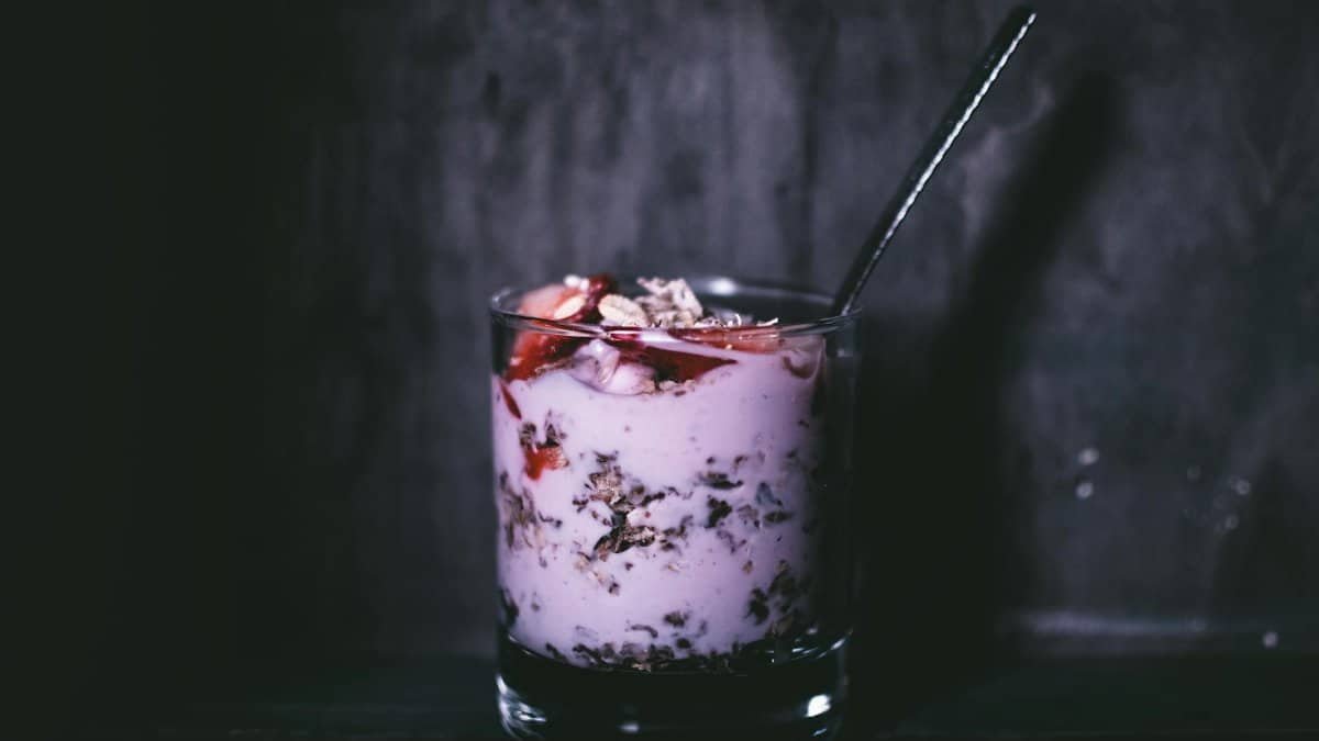 Dark, moody close-up of a delicious yogurt parfait with granola and berries in a glass.