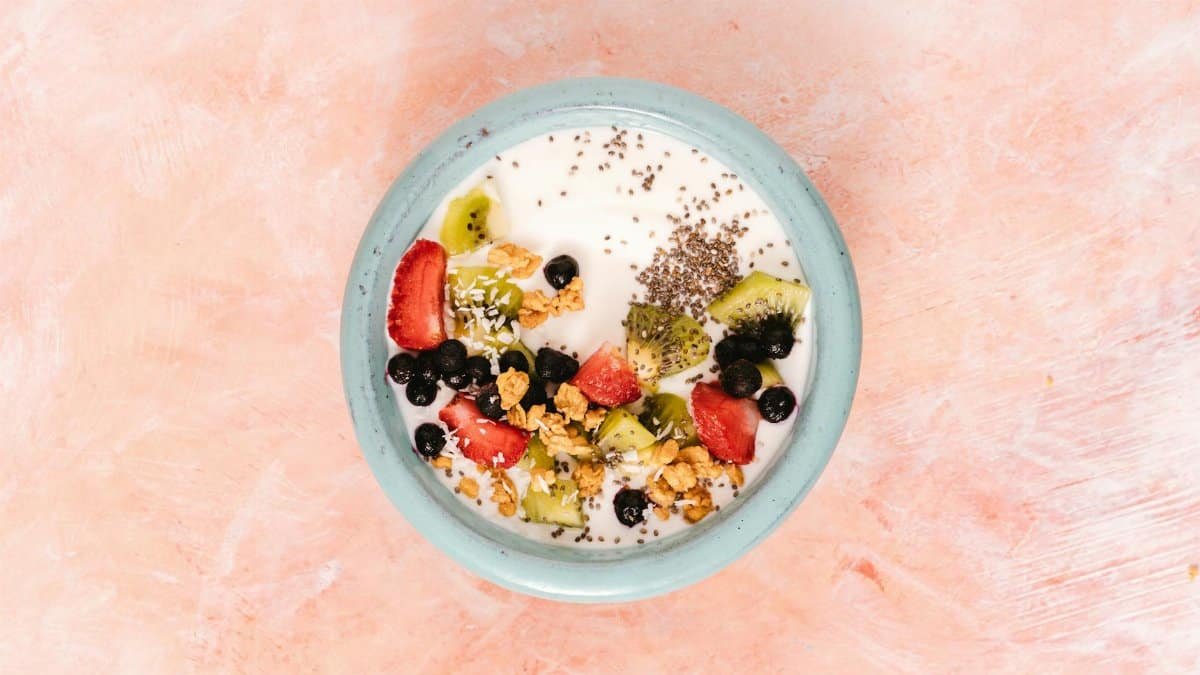 Top view of a nutritious breakfast bowl with yogurt, fresh fruits, and seeds on a pink background.