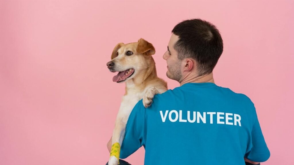 A cheerful volunteer holding a happy dog against a pink background.