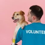 A cheerful volunteer holding a happy dog against a pink background.