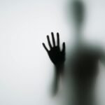 Abstract silhouette of person with hands against glass, creating a mysterious vibe.