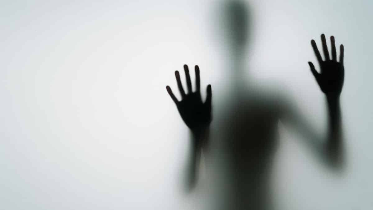 Abstract silhouette of person with hands against glass, creating a mysterious vibe.