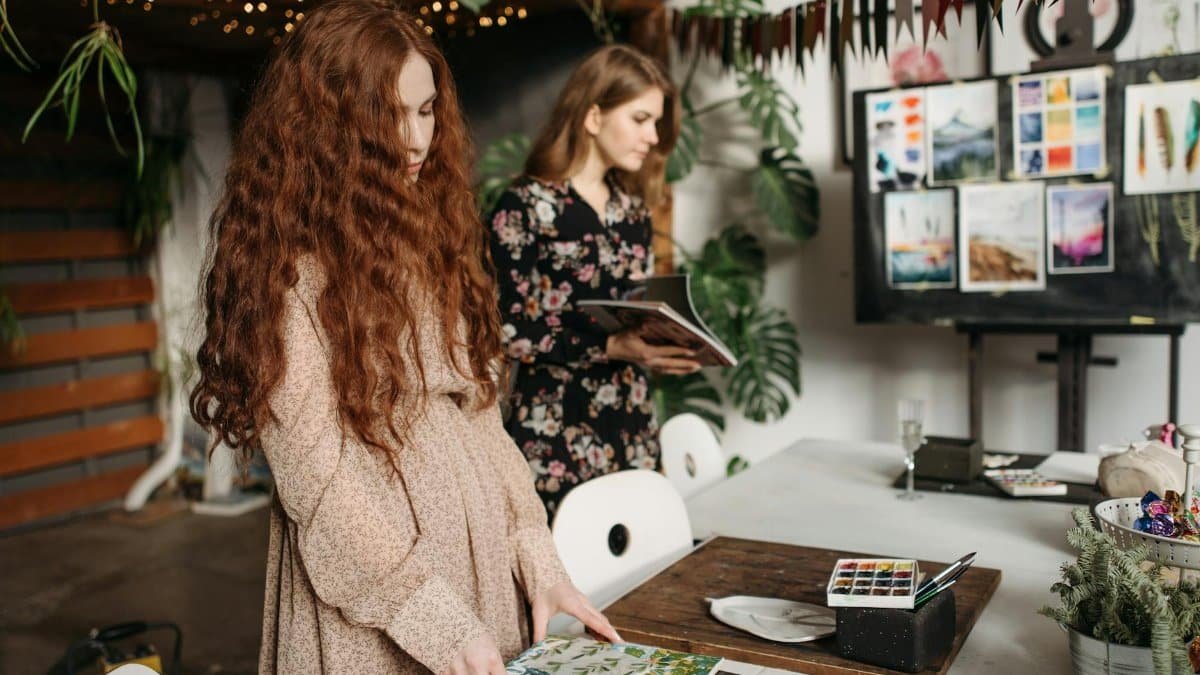 Young women engage in an art workshop surrounded by paintings and plants.