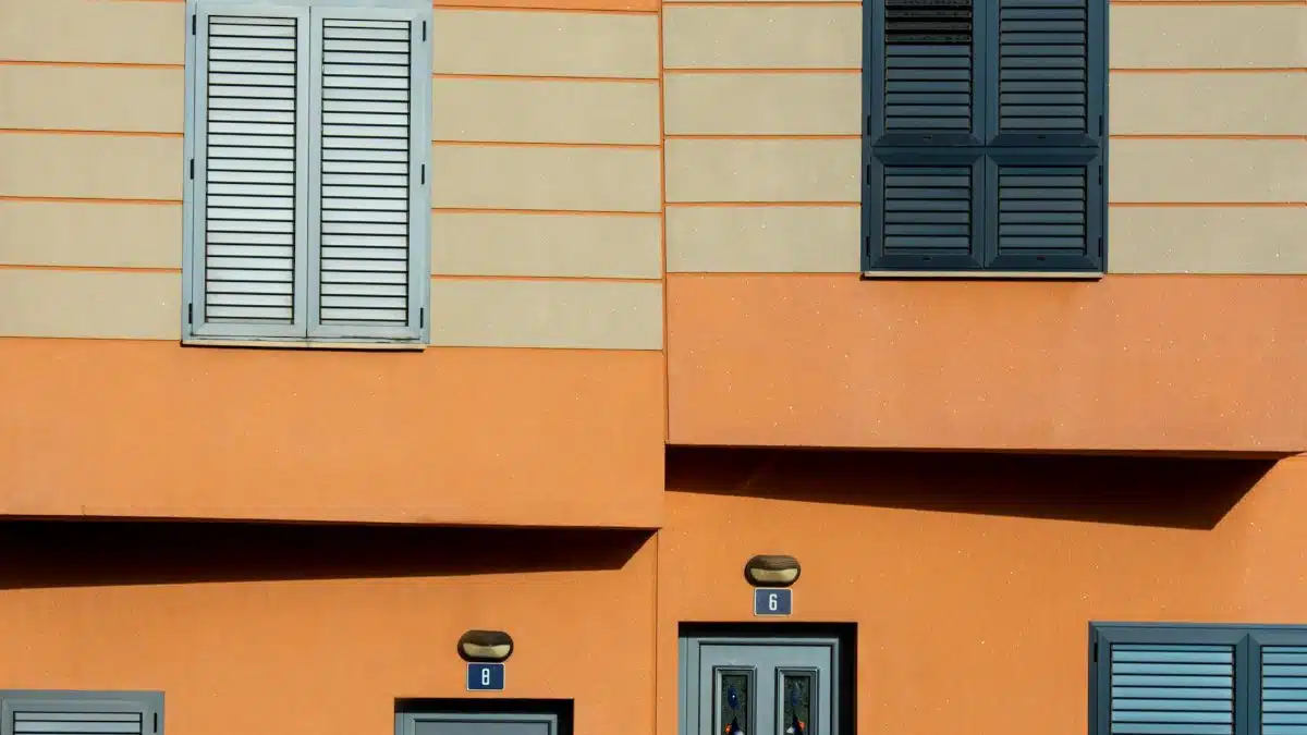 Close-up of a sunlit orange residential building facade with shutters and doors.