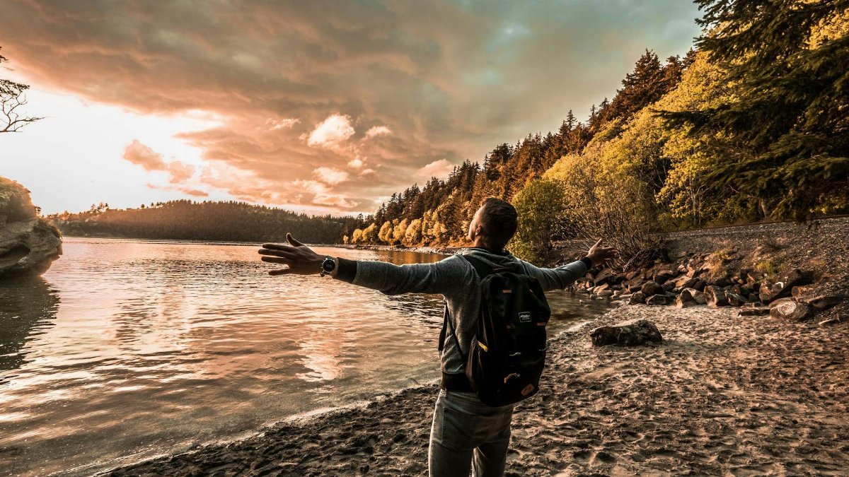 Man with arms outstretched, enjoying a scenic sunset by a lakeside in Bellingham, WA.