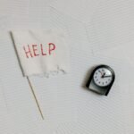 A flat lay image depicting stress and overwork with a help flag and clock on papers.