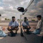 Father and son kneeling together outdoors, learning car maintenance with tools.