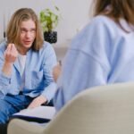 A young man in therapy, gesturing towards therapist in a comfortable setting.