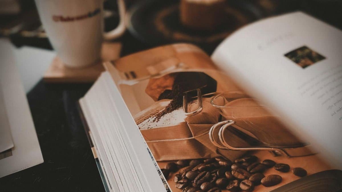 Warm coffee shop setup with an open book, latte, and cake, perfect for relaxation.