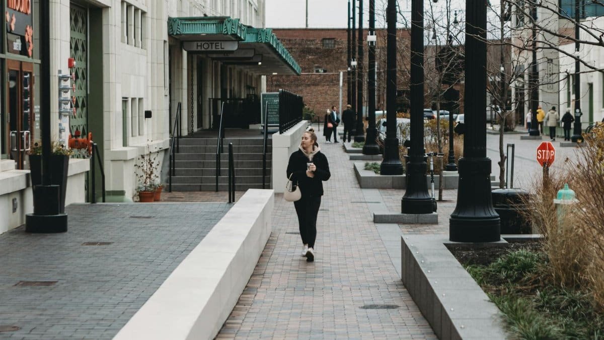 Woman walking with coffee on a city street showcasing urban architecture and lifestyle.
