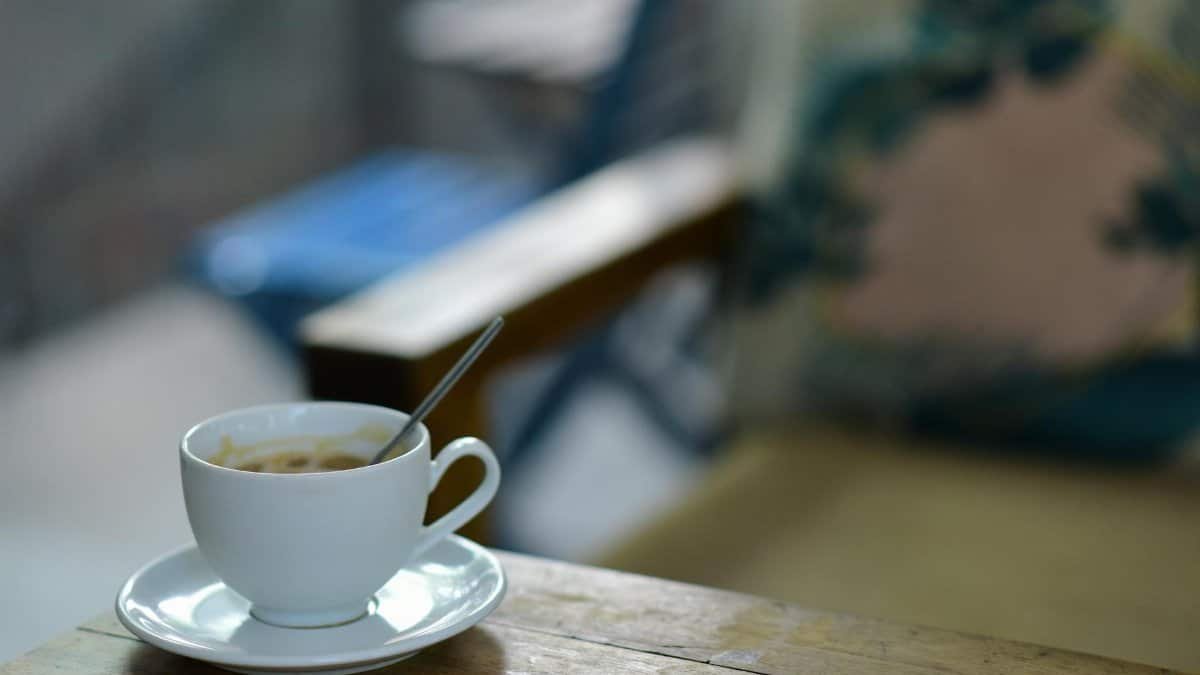 A warm cup of coffee rests on a wooden table in a cozy, relaxing outdoor setting.