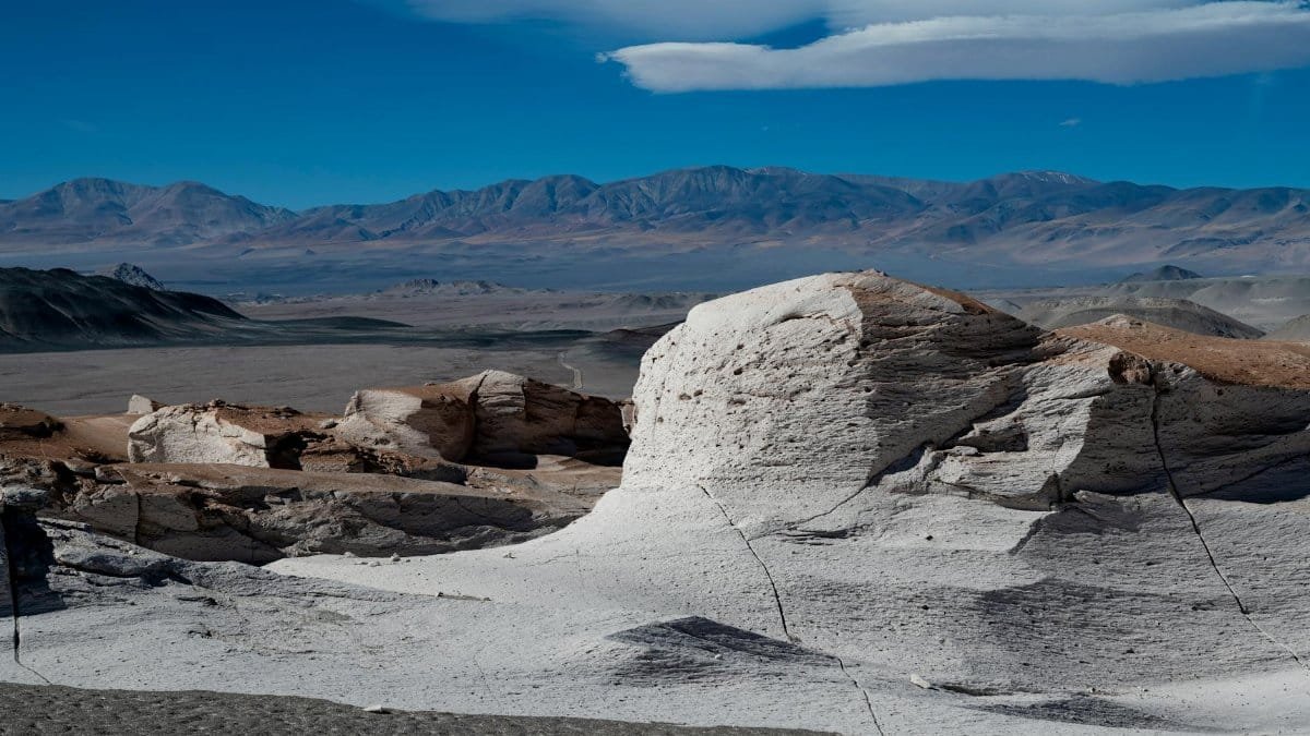 Beautiful desert scene with unique rock formations and distant mountains under a vibrant blue sky.