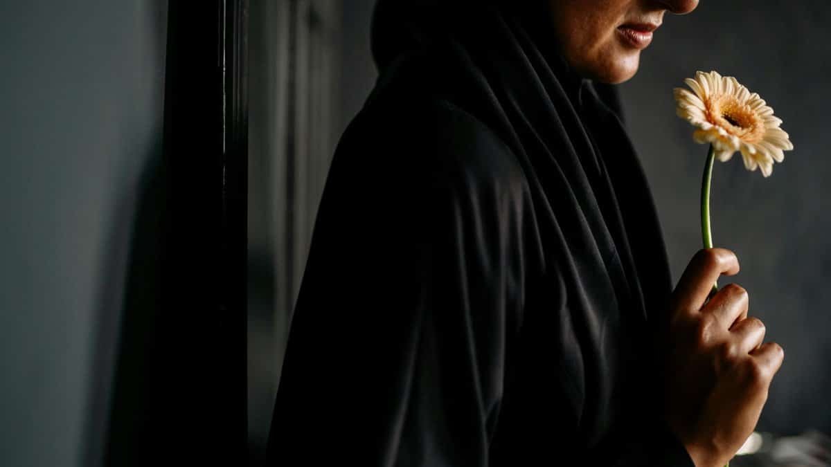 A woman in dark attire holds a single gerbera indoors, exuding elegance and serenity.