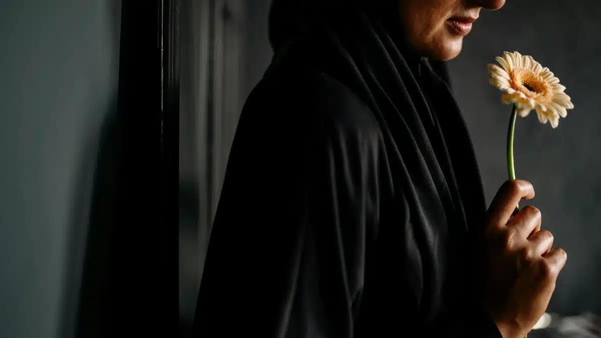 A woman in dark attire holds a single gerbera indoors, exuding elegance and serenity.