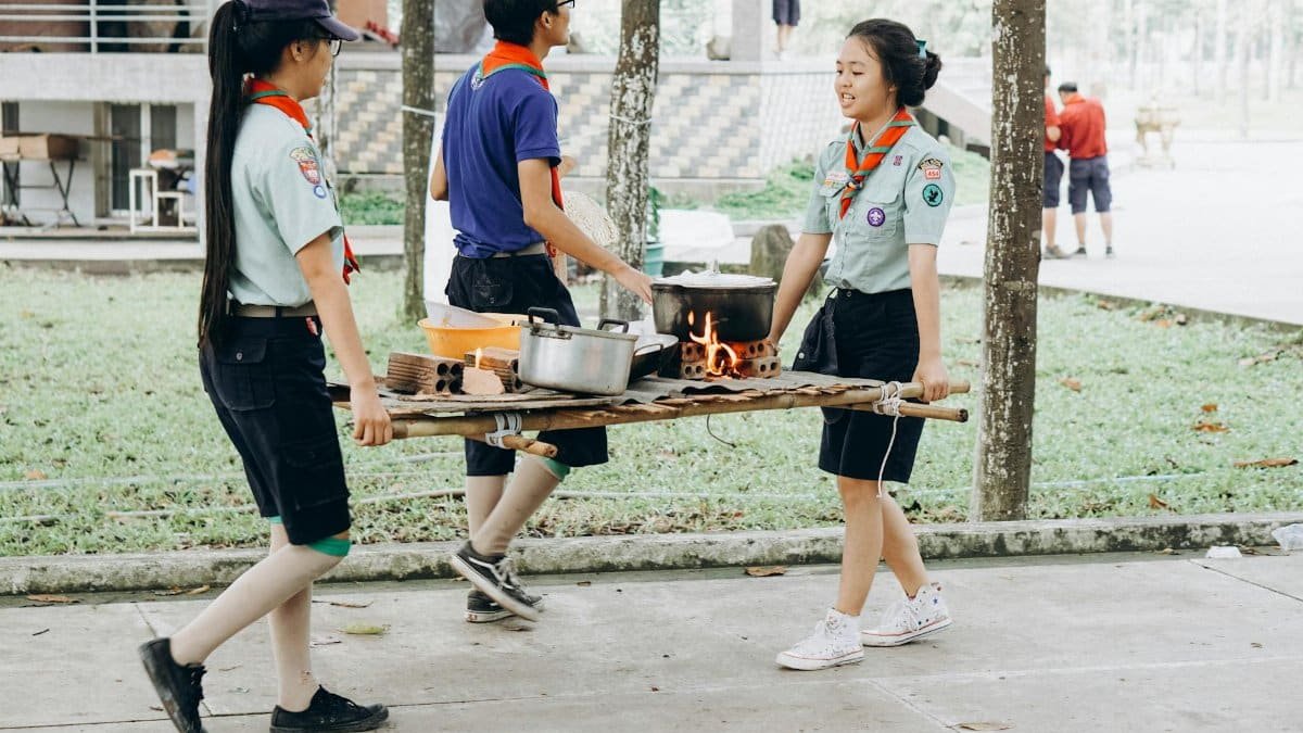 Youth scouts engaging in an outdoor cooking activity, carrying food and pots.