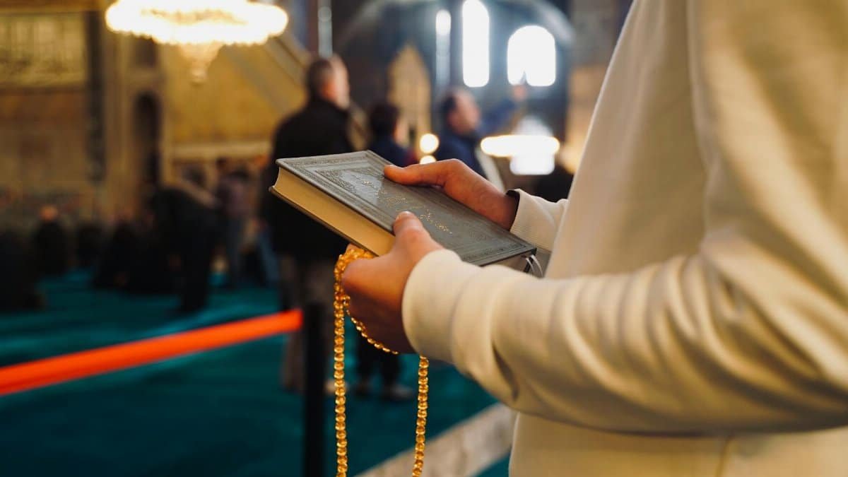 A person holding a Quran and prayer beads inside a mosque in Istanbul, Türkiye.