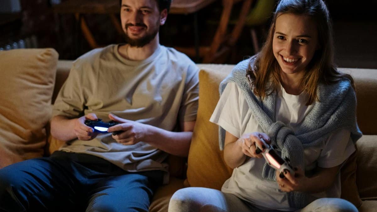 Smiling couple playing video games on couch at night, sharing joyful moments.