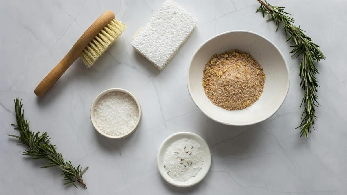 Top view of bowls with ingredients for organic scrub arranged with pumice stone and fresh branches of rosemary