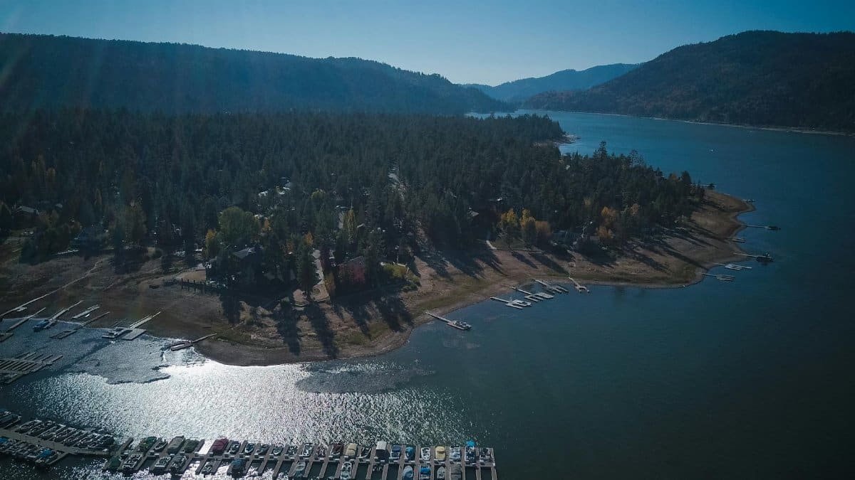 A breathtaking aerial view of a tranquil lakeside surrounded by lush forests and hills under clear blue skies.