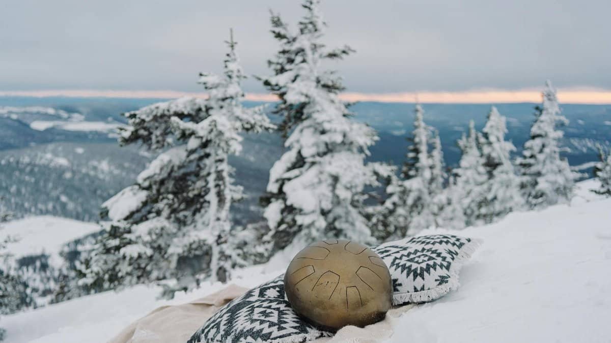 Snowy mountain landscape with a meditation setup including a metallic drum and patterned cushion, evoking tranquility.