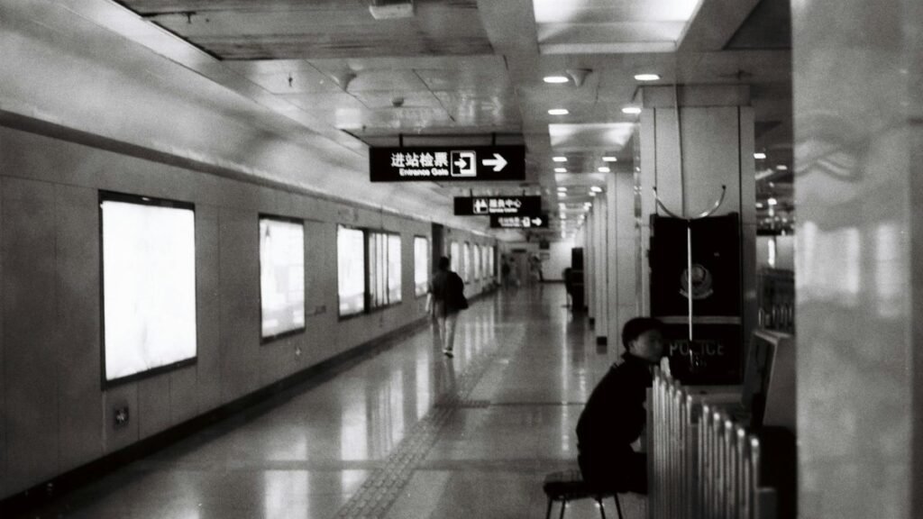 A black and white photo of a subway station corridor with signs and people walking.