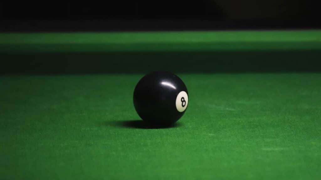 Close-up of black eight ball on a green billiard table with soft lighting.