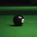 Close-up of black eight ball on a green billiard table with soft lighting.