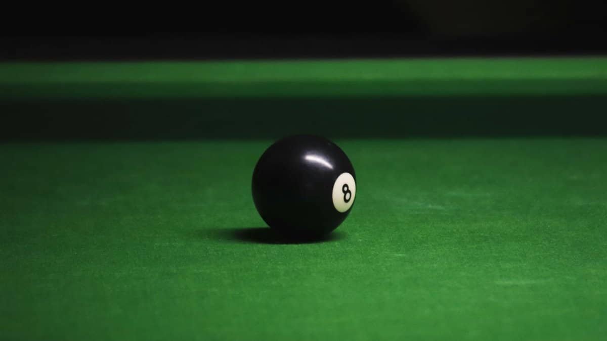 Close-up of black eight ball on a green billiard table with soft lighting.