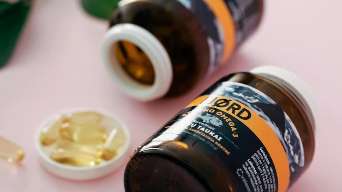 Close-up of Omega-3 fish oil capsules in transparent bottles on a pink background.