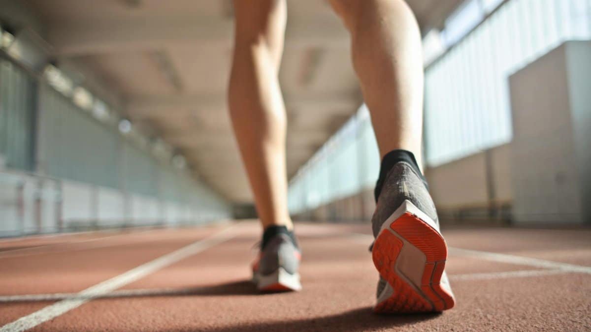 Back view of a runner's legs in a stadium, focusing on footwear and athletic motion.
