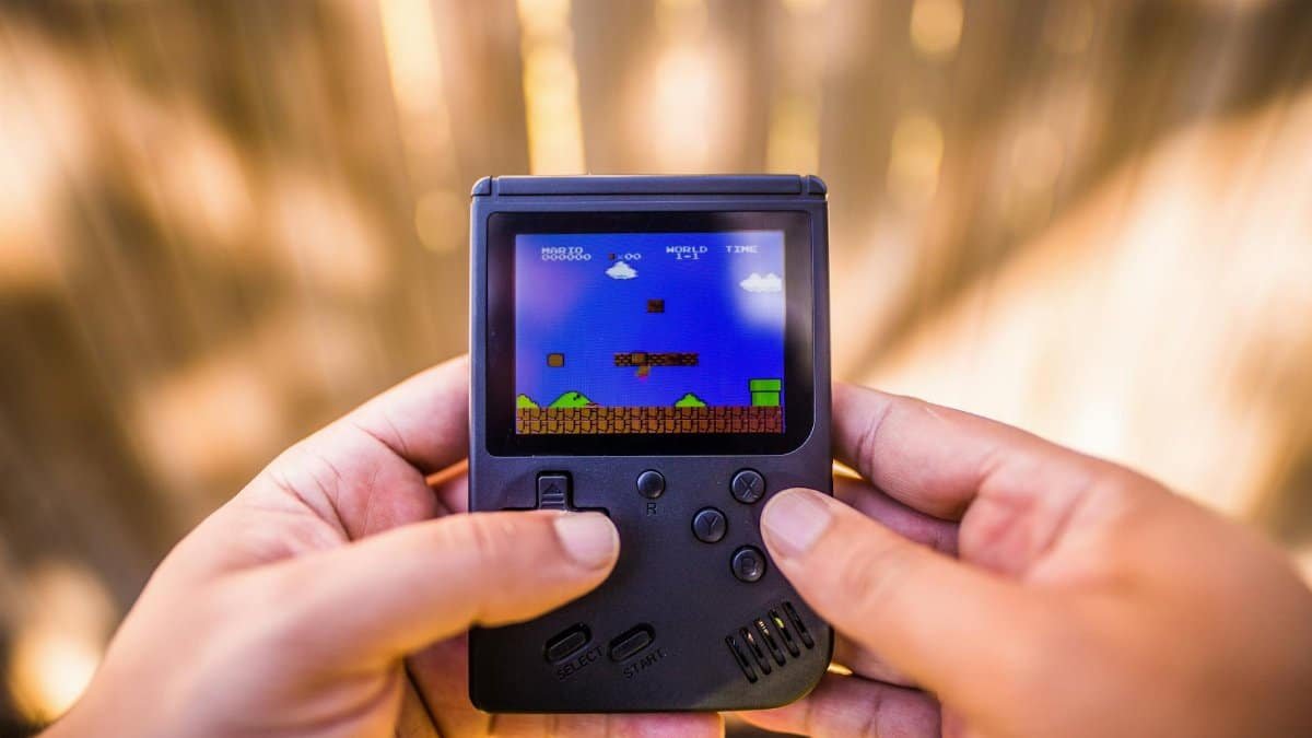 A close-up of hands holding a retro game console playing a classic Mario game outdoors.
