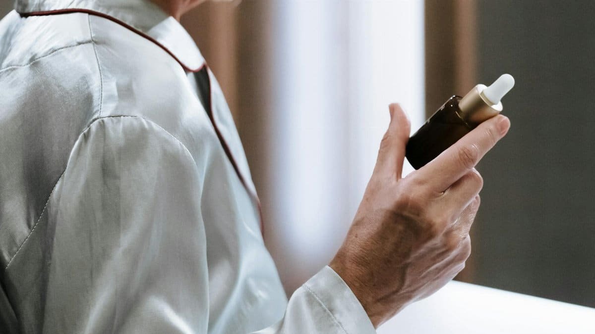 Close-up of a person holding a serum dropper bottle, highlighting skincare routine and self-care.