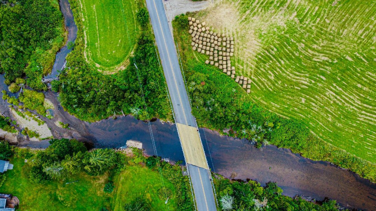 Drone shot of a bridge over a river in rural Nova Scotia, surrounded by fields.