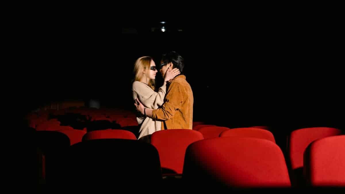 Couple sharing a tender moment in an empty movie theater with red seats.