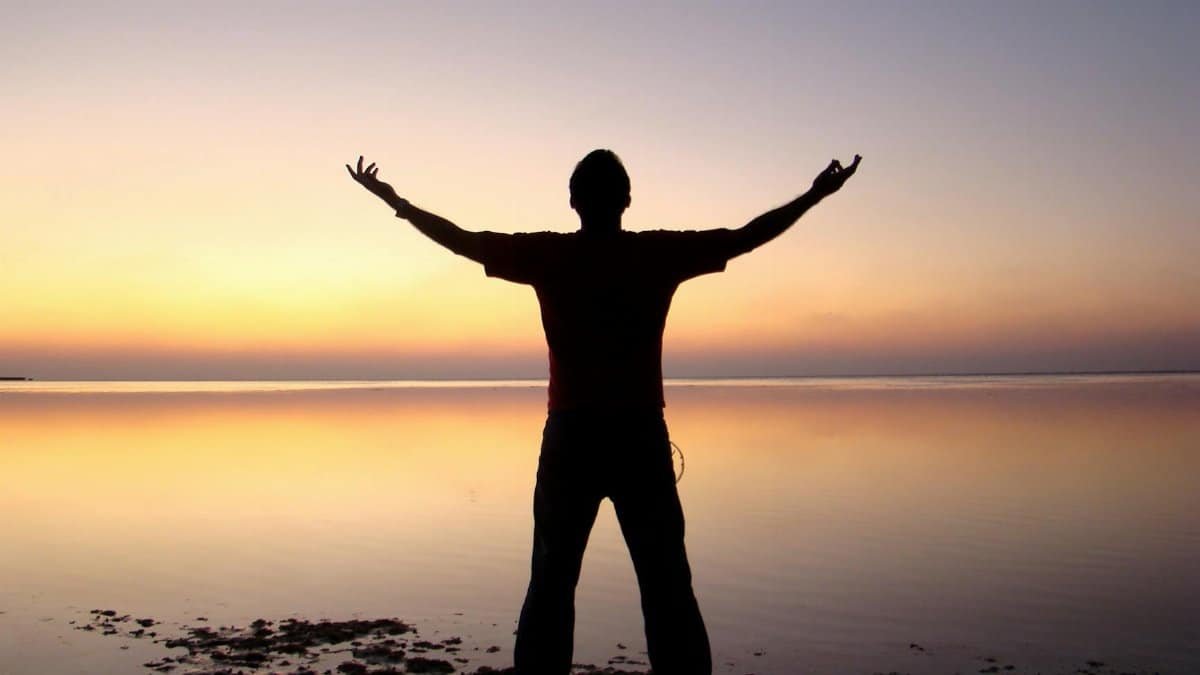 A person joyfully embracing the sunrise over a calm ocean, symbolizing freedom and solitude.
