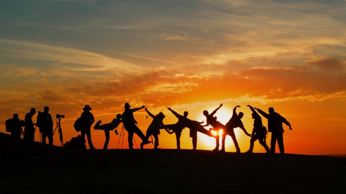 Group of people silhouetted against a vibrant sunset, showcasing unity and joy.
