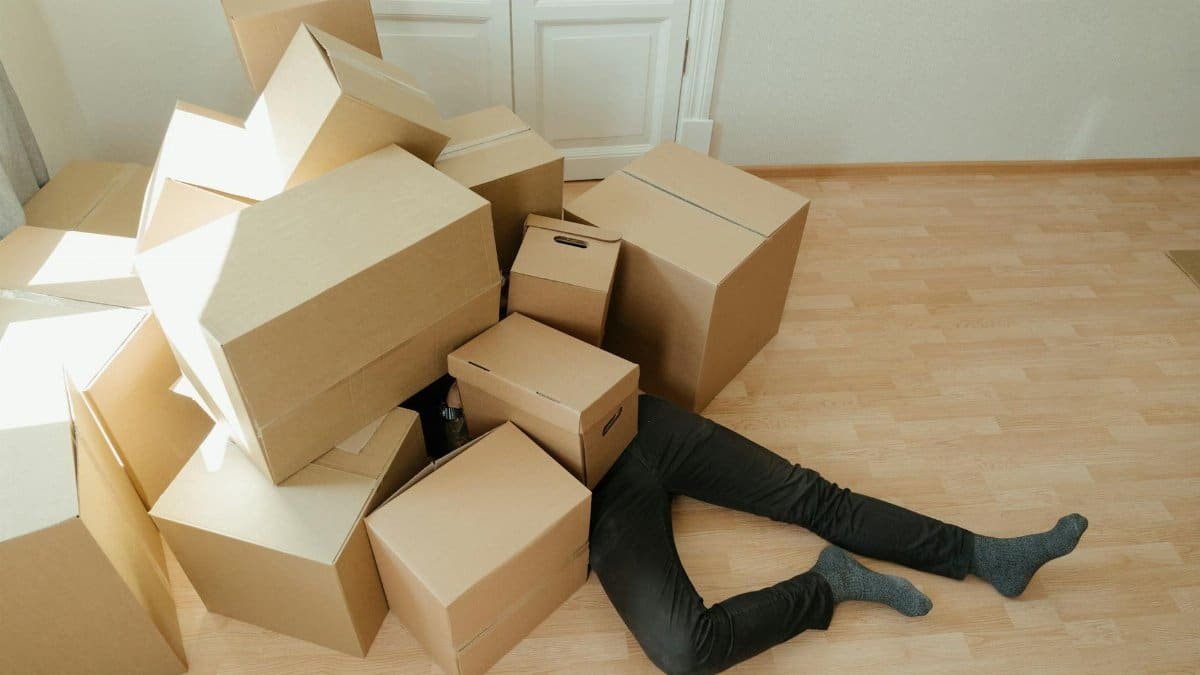 A person overwhelmed by cardboard boxes during a home move, symbolizing stress and relocation.