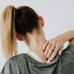 A woman in casual clothing holds her neck, indicating pain or discomfort.