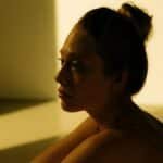 Side view of a woman reflecting in warm sunlight indoors, creating a serene and introspective mood.